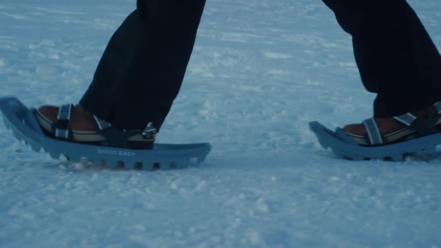 A person wearing a pair of snow shoes walks across a snow covered landscape