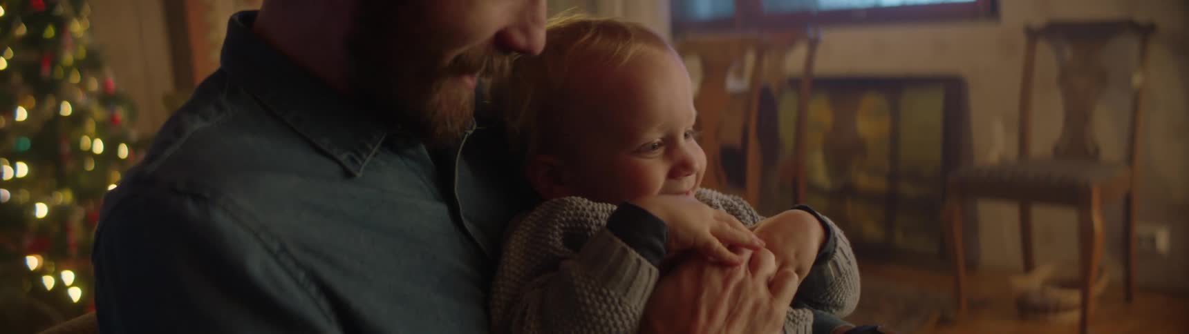 Father playing with his son on his arms in the living room near a christmas tree
