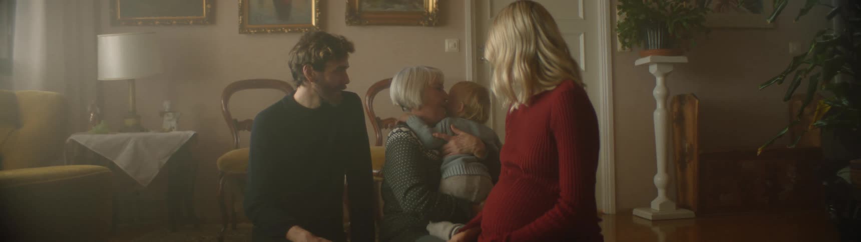 A young boy runs and jumps in to his grandmothers lap as his parents watch and laugh