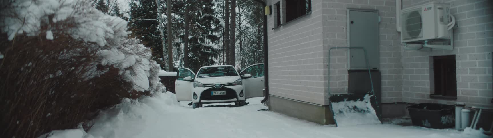 A family parking a car on the side of a house covered in snow close to a forest at winter