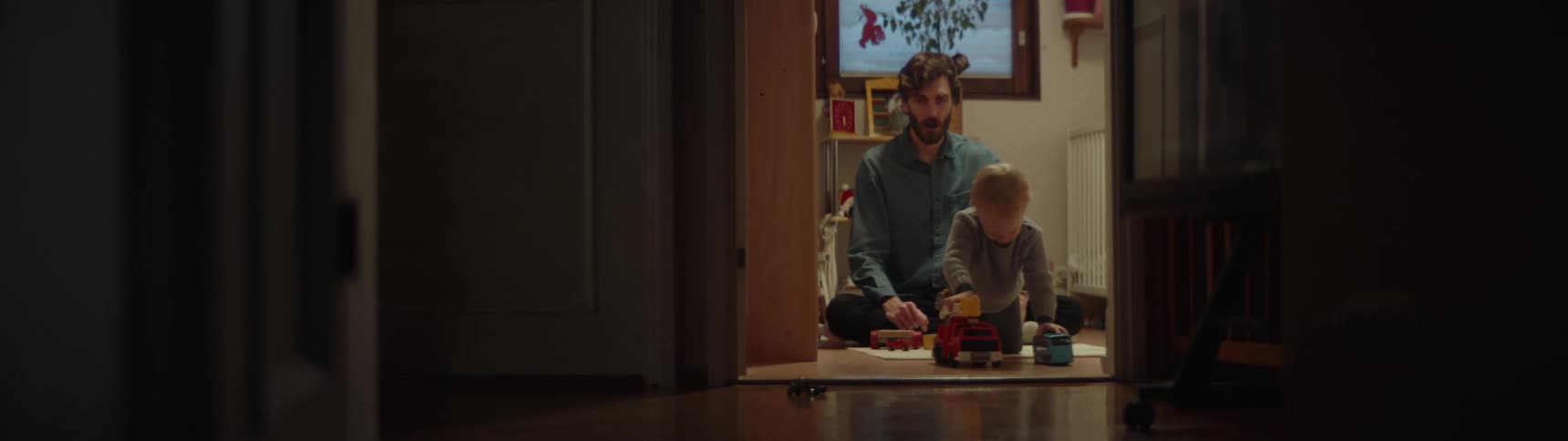 A man sits on the floor while his son plays with toys