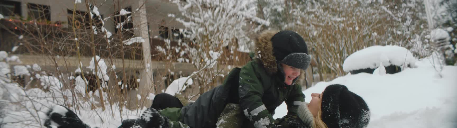 Family wearing thick winter clothes playing with snow on the ground near a house at winter