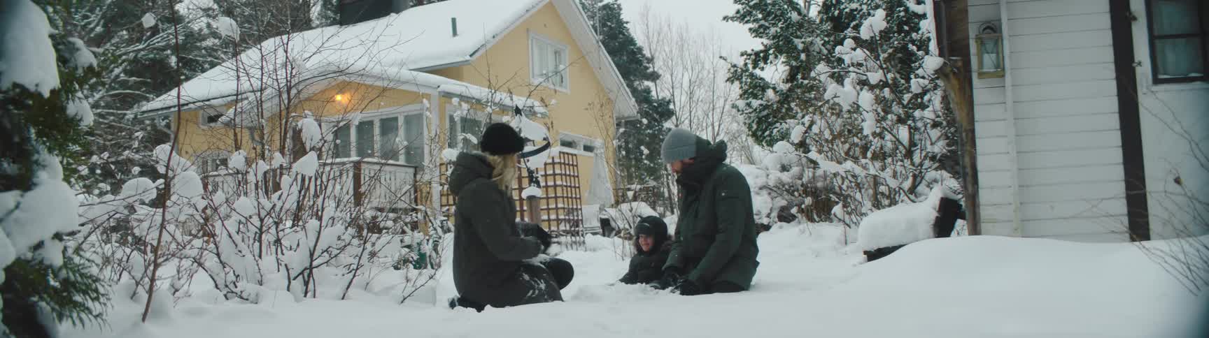 Three children sit in the snow in the yard