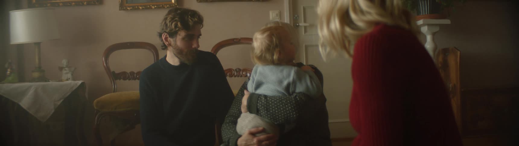 A little boy climbs in to his grandmothers lap as his parents watch and reach out and touch him