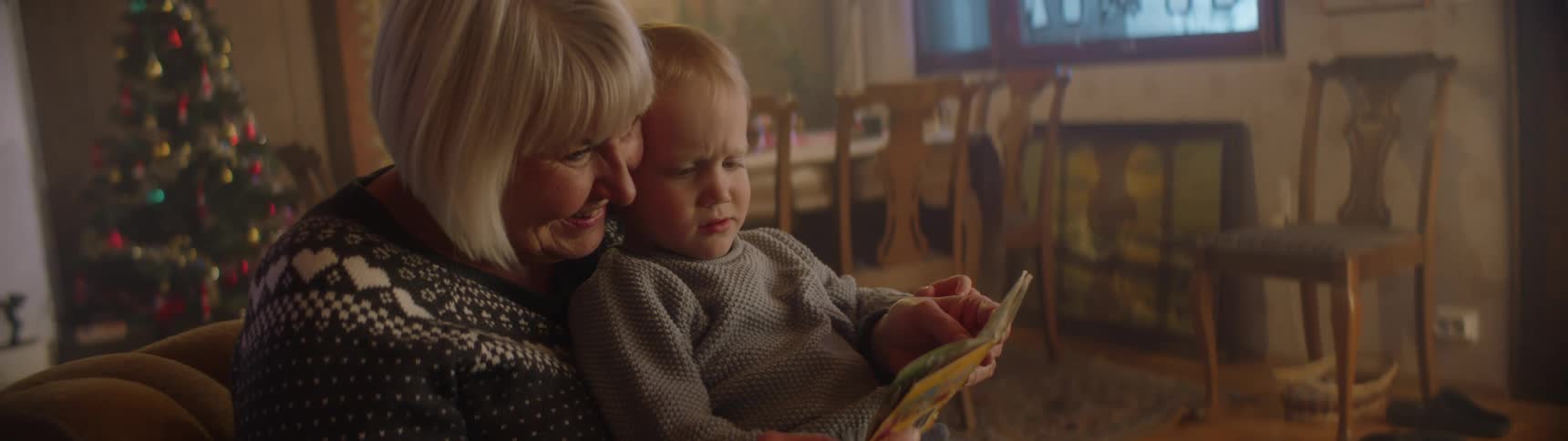 Grandmother reading a story to her grandson on the living room at home near a christmas tree