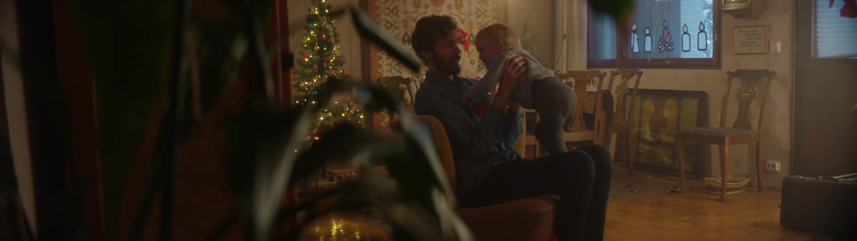 A man at home picks up his young son and puts him on his lap