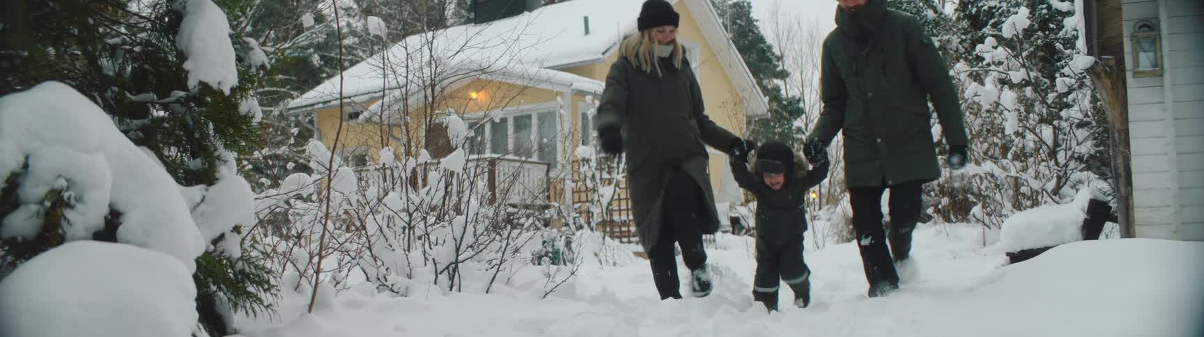 A mother and father playfully each hold the hand of their young child as the three of them run through the snow