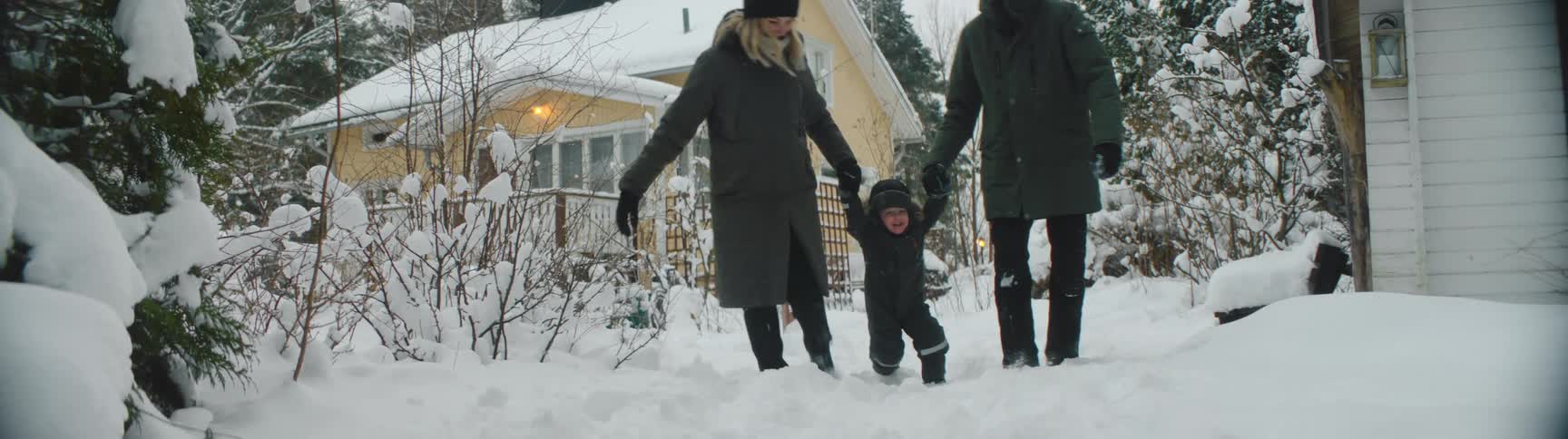Family wearing thick winter clothes playing on the snow near a house at winter