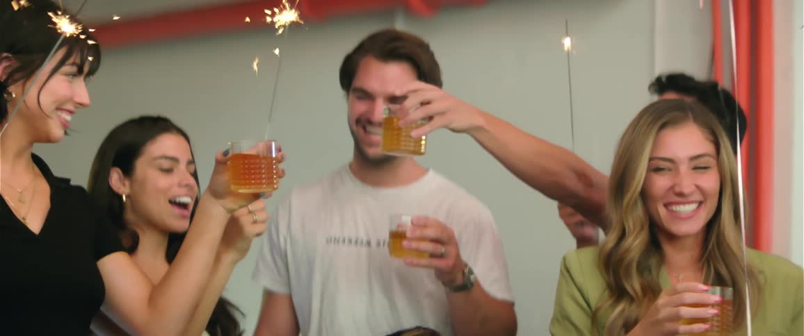 Group of friends holding sparklers and drinks on their hands celebrate a birthday