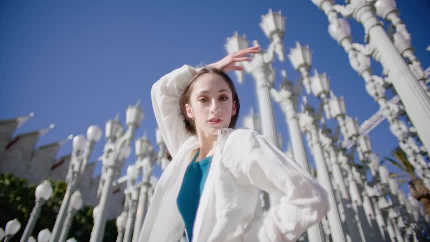 A female dancer performs a series of dance moves outside in front of several lamp posts