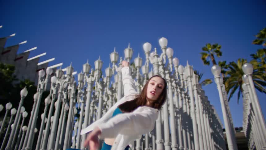 A woman performs a modern hip hop dance in front of rows of lamp posts