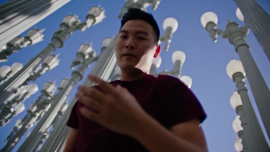 An asian male dancer performs dance moves outside near numerous lamp posts