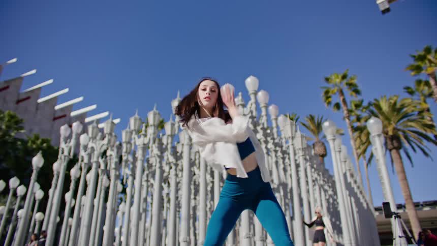 A woman dances hip hop style in front of an art display of lamp posts