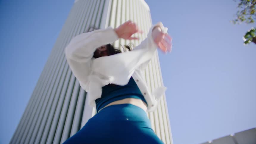 A young woman dances over a camera in a city on a clear day