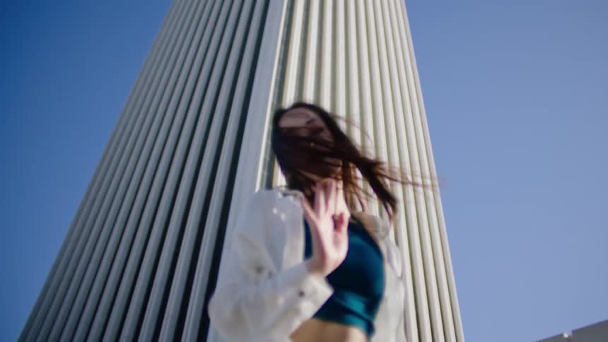 A female dancer performs a series of dance moves while outside and in front of a tall building