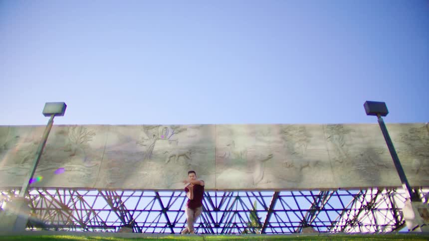 Young asian man energetically dancing in front of a metallic structure under a blue sky