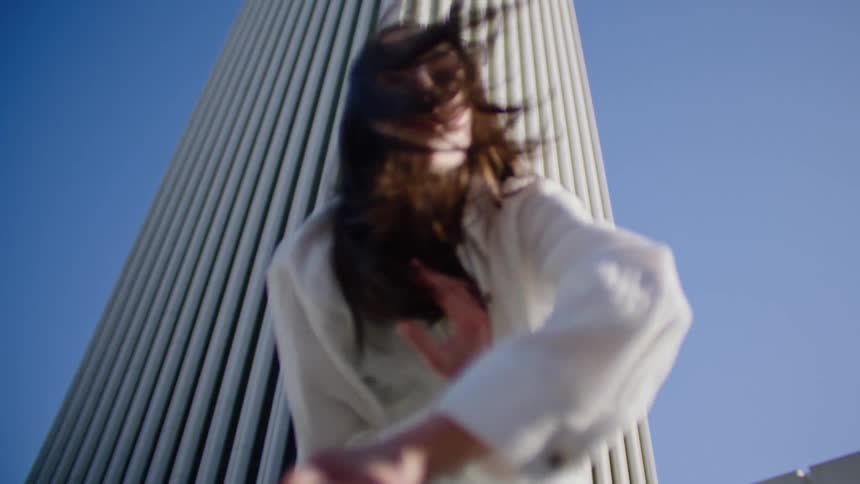 A female performs a series of dance moves outside in front of a tall white building
