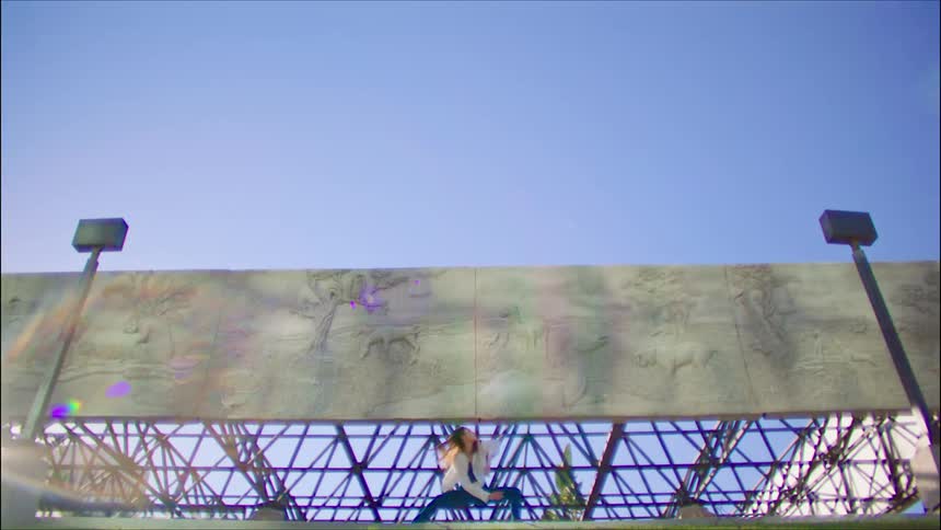A female dancer performs flamboyant dance moves while outside near a large mural