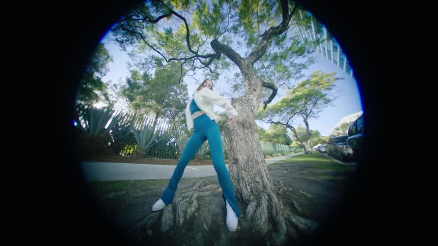 A woman dances in front of a tree at the end of her driveway