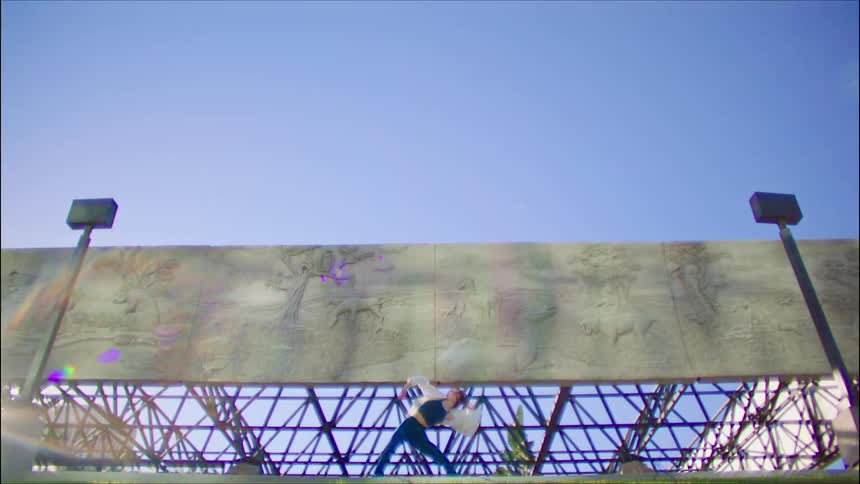 Female dancer with white shirt and teal top and pants dances in front of monument with motifs