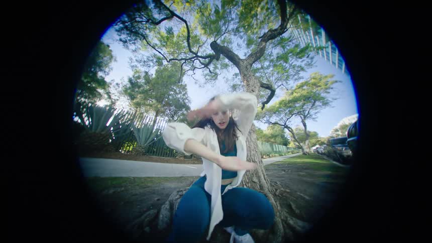 A woman dances in front of a tree in a neighborhood
