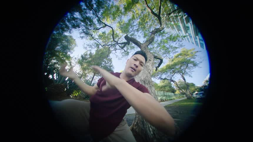 Young asian man energetically dancing in front of a tree in a park at morning seen through a fisheye lens