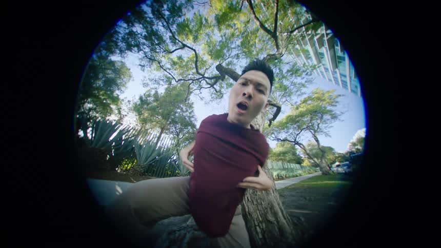 Young asian man energetically dancing in front of a tree in a park at morning seen through a fisheye lens