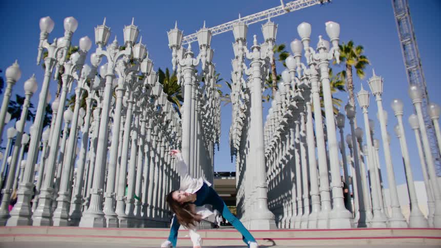 A female performs a series of dance moves outside near numerous lamp posts