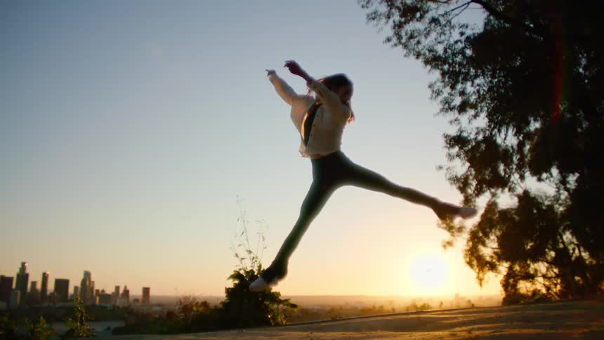 Dancing woman wearing white shirt and black trousers is silhouetted against the sunset
