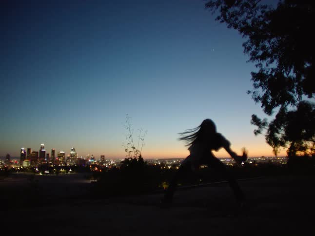 Silhouette of a woman dancing with the view of a metropolis skyline at the background during sunset