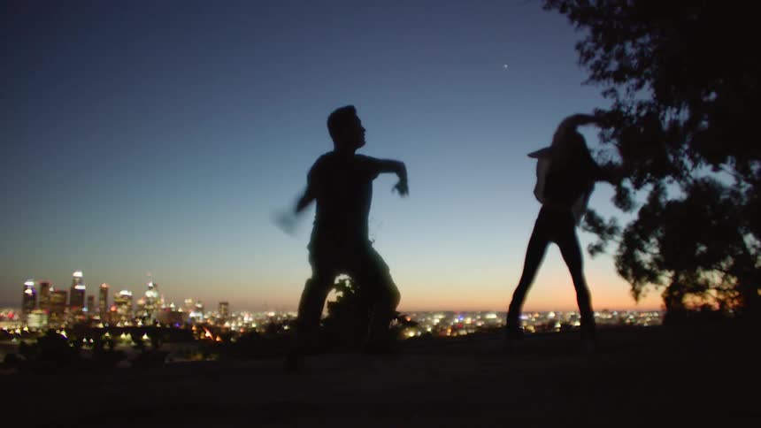 Silhouette of a man and a woman dancing together during the sunset with the view of a big city in the background