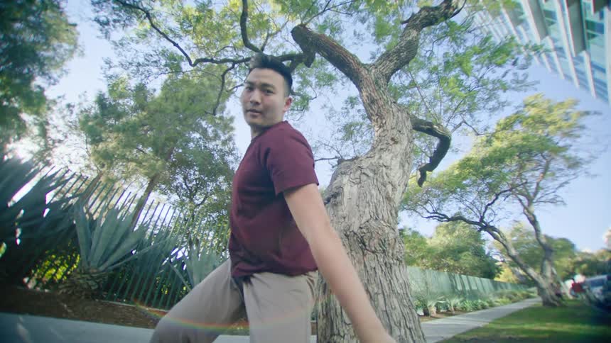 Young asian man energetically dancing in front of a tree in a park at morning