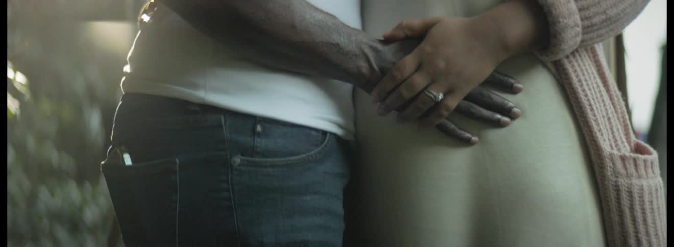 A man holds hands with his wife and touches her pregnant stomach