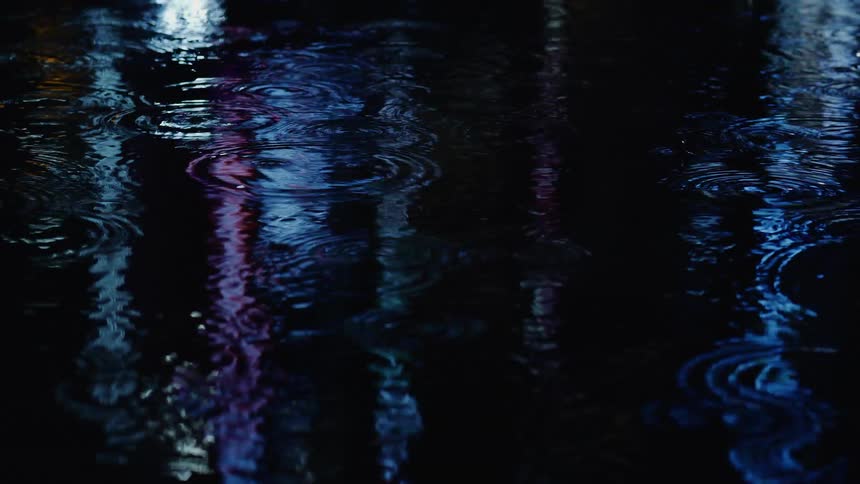 City lights reflecting on a pool of water under the rain at night
