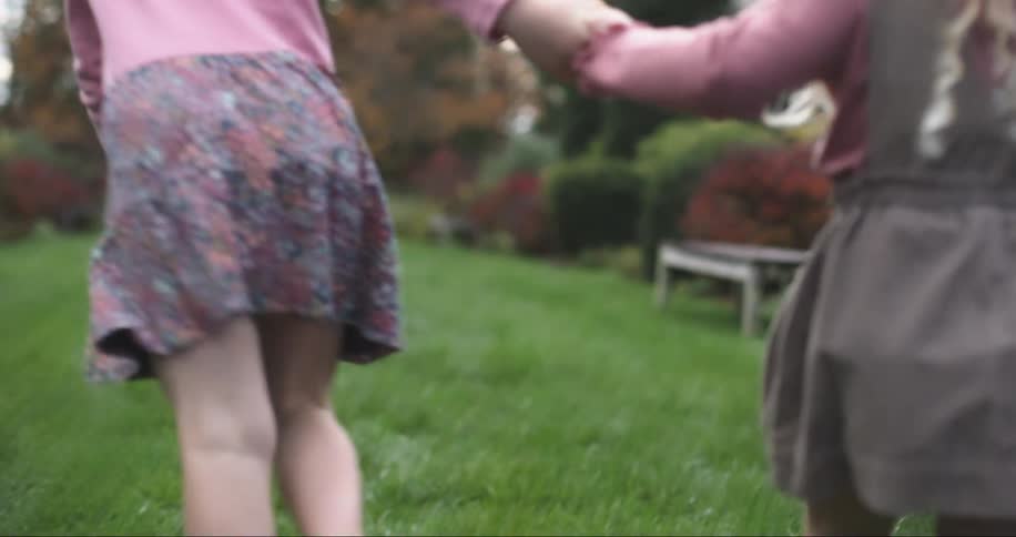 Two little girls climb steps and hold hands running through a garden with fall color