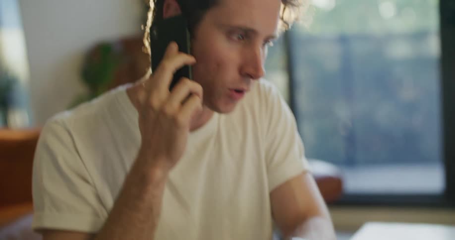 Man working from home takes a call on his smartphone in the morning
