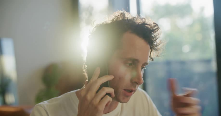Man works in home office consulting laptop as he talks on a mobile phone
