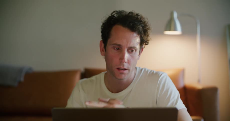 Tired man yawning and using his laptop indoors in front of a couch