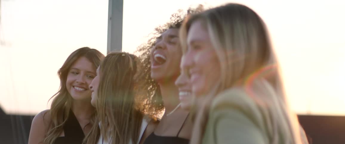 Five female friends standing together outdoors laughing and smiling while posing for a picture