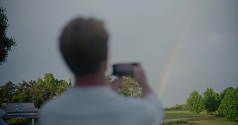 Man takes pictures of rainbow over a field using a mobile phone