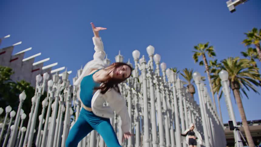 A woman writhes back and forth while dancing in front of a display of lamp posts in deep rows