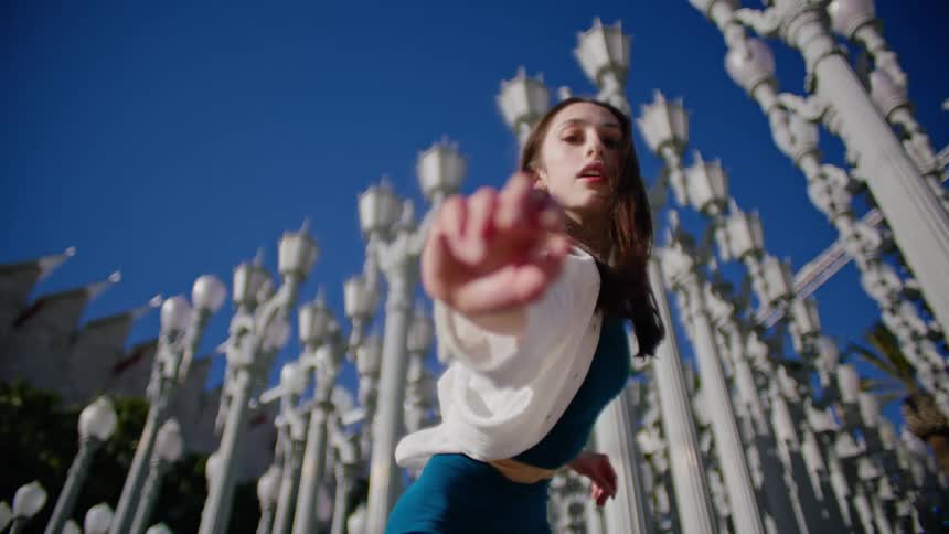 Young woman energetically dancing in front of street lamps on a park in the city