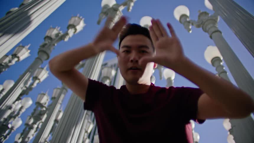 Young asian man energetically dancing in front of a street lamps on a park under a blue sky