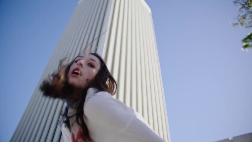 Female dancer with white shirt and teal top and pants dances in front of white skyscraper