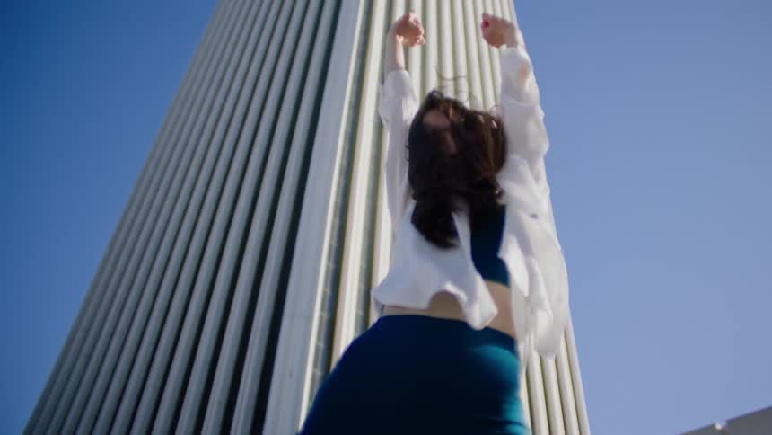 Female dancer with white shirt and teal top and pants dances in front of white skyscraper