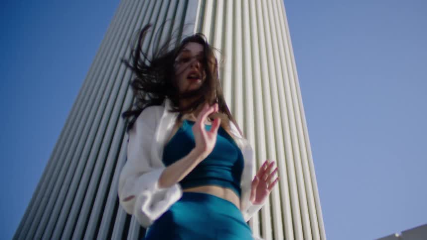 A beautiful female dancer performs dance moves beneath a very tall building