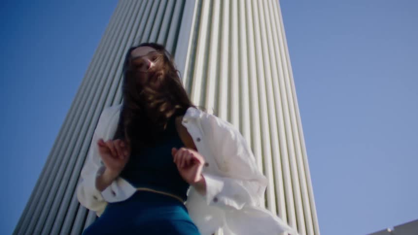 Woman dances at base of architecturally detailed tower on clear day