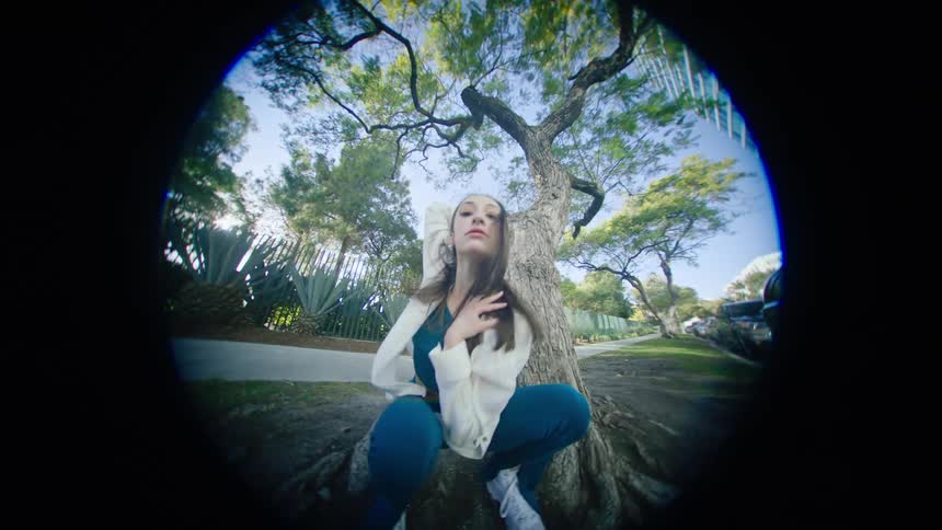 Young woman energetically dancing in front of a tree in a park at morning seen through a fisheye lens