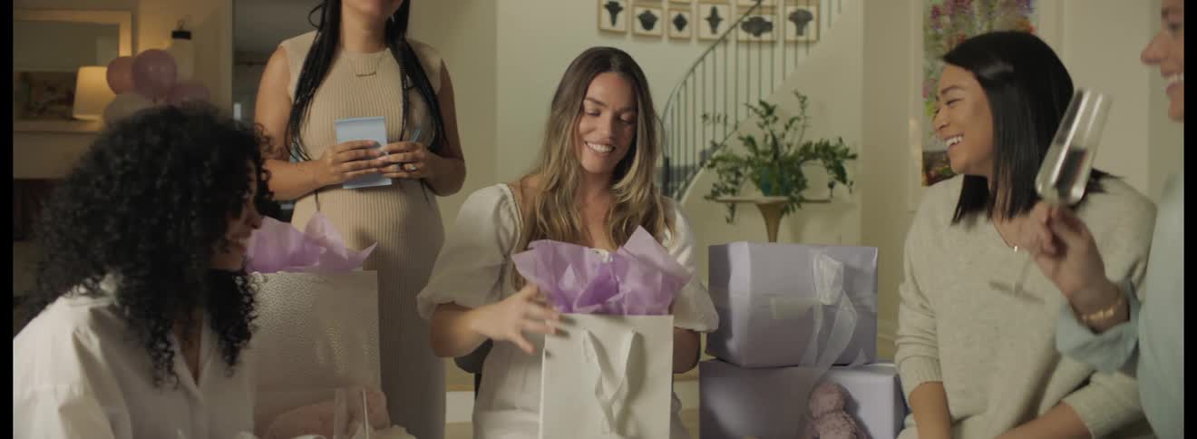 Pregnant women opening gifts at baby shower as friends watch