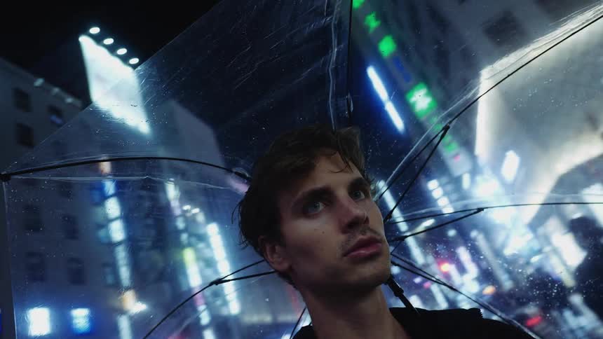 Man holding transparent umbrella looks around in downtown street at night in the city